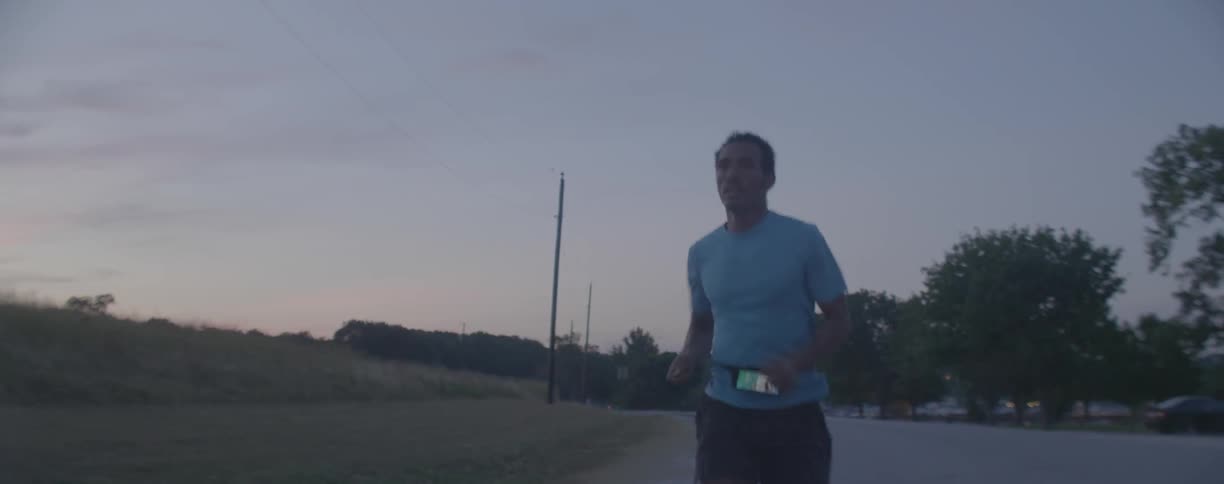 Man runs down a road next to a field under a cloudy sky