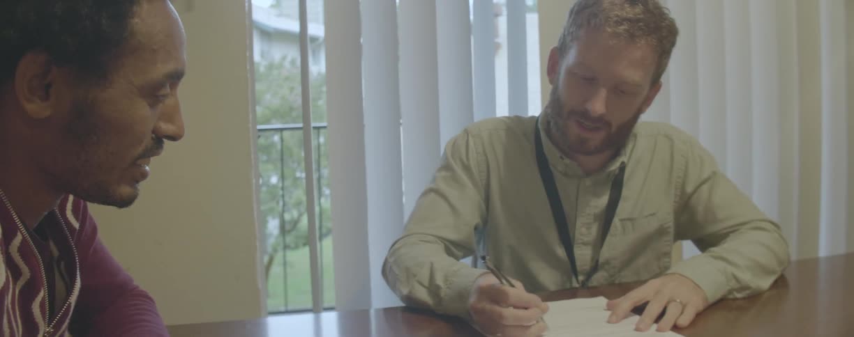 Two men talk while filling out a form at home