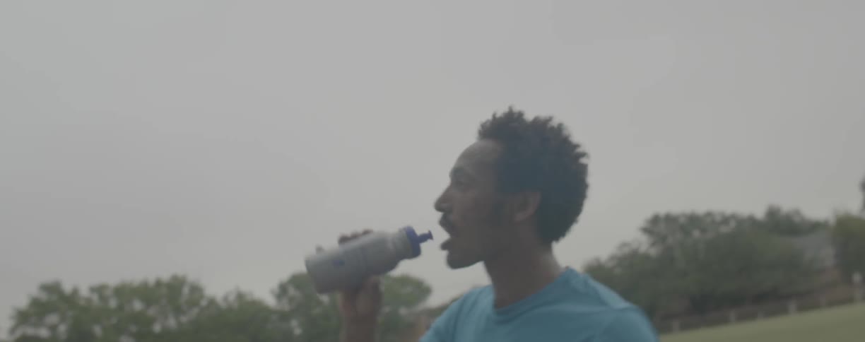 Man hands another man a bottle of water on the track