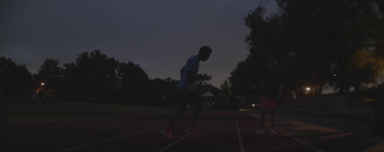Two men exercise on an outdoor race track at dusk