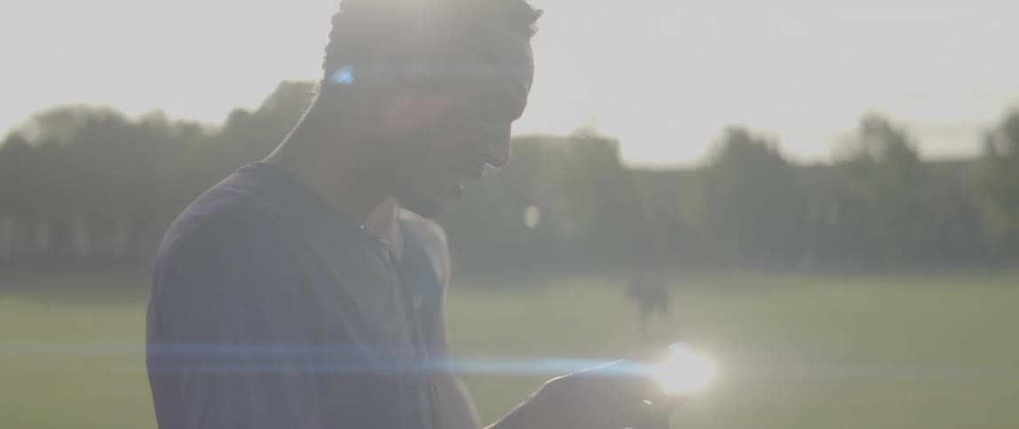 Man touches his cellphone as he stands in a field on a sunny day