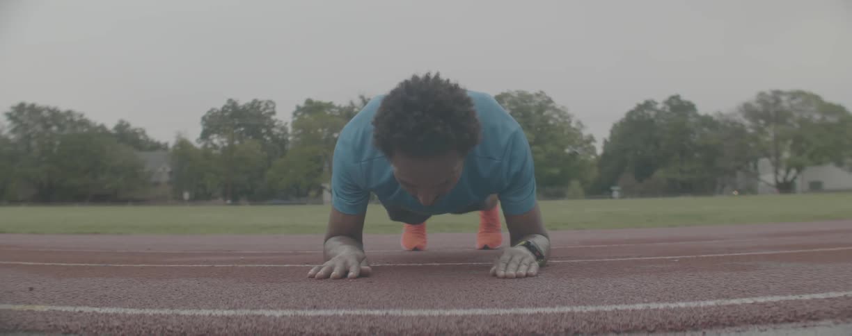 Man is doing plank on running track on overcast day