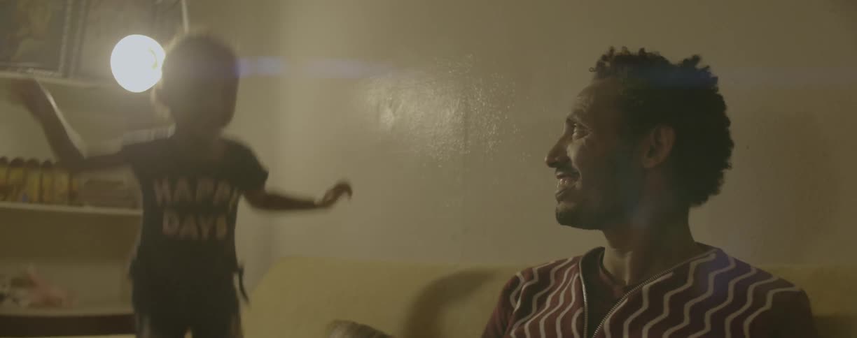 Man smiles as little girl jumps on bed in room