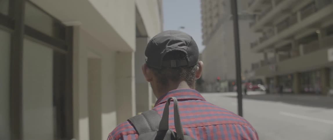Man wearing backpack is walking on city street on sunny day