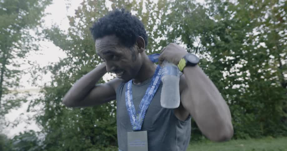 A runner smiles while putting on a medal