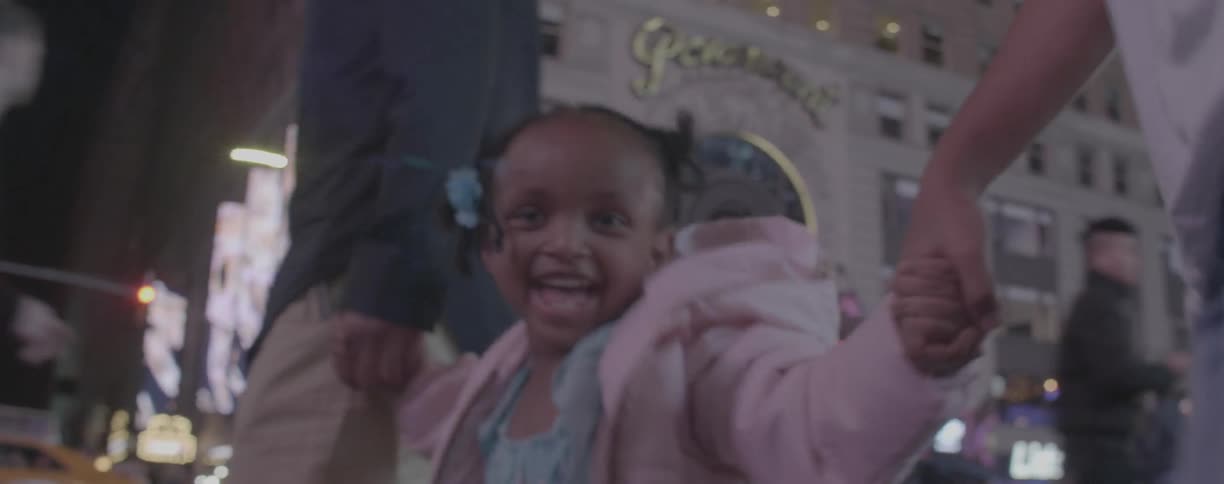 A young girl smiles while holding hands with her parents on a sidewalk