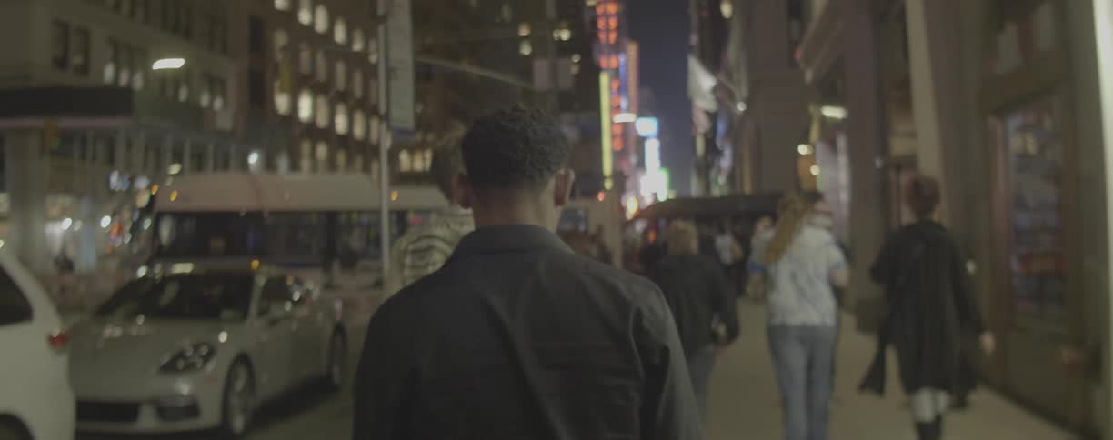 Pedestrians walk on a city sidewalk at night