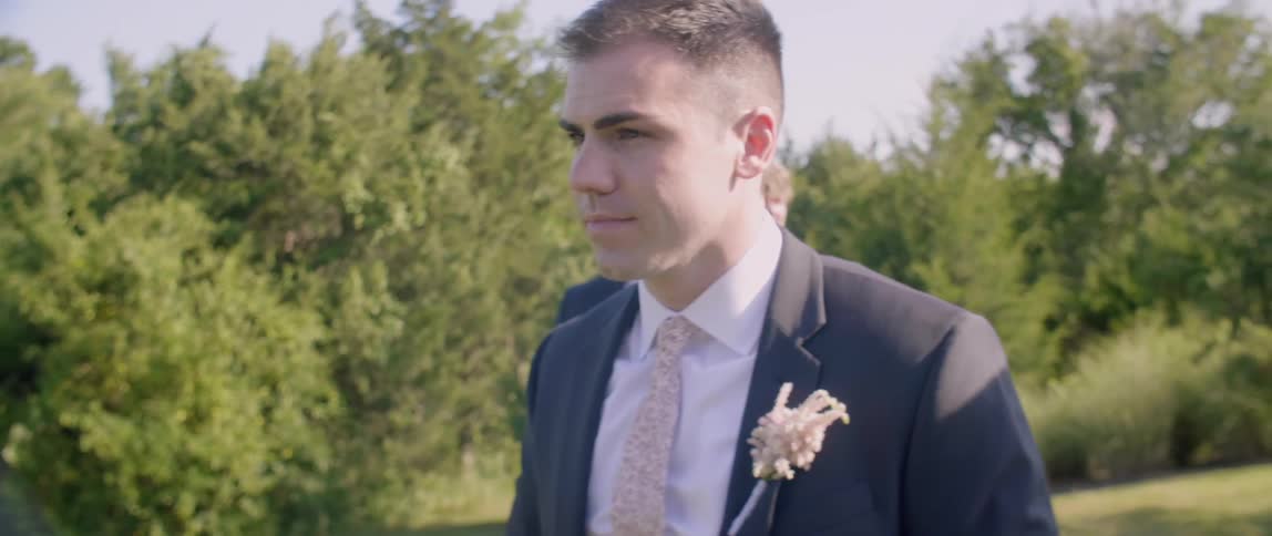 Groom stands outside on sunny day