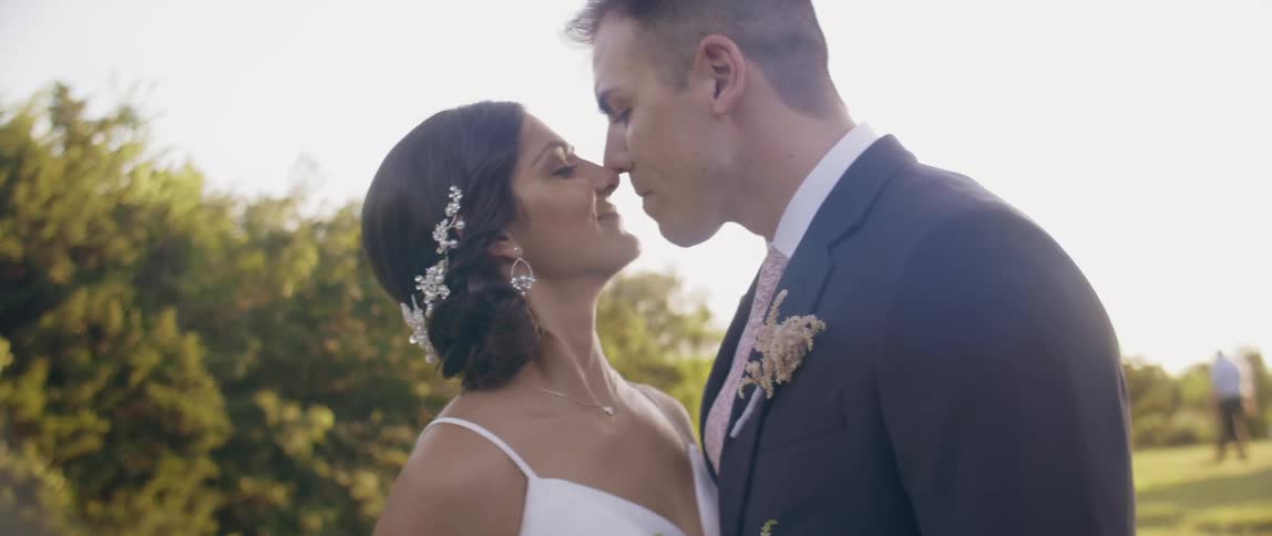 Bride and groom embrace and kiss outside on sunny day