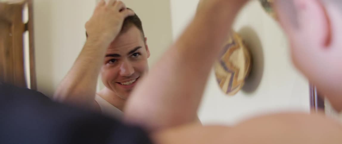 A man smiles while styling his hair