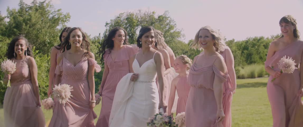 Bride and bridesmaids are smiling and walking outside on sunny day