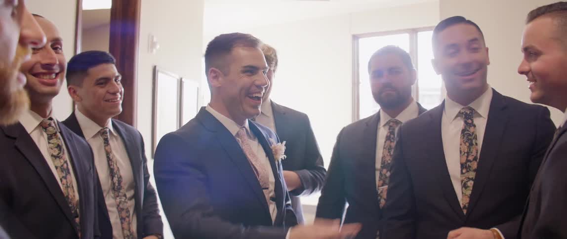 A groom surrounded by his groomsmen points and laughs