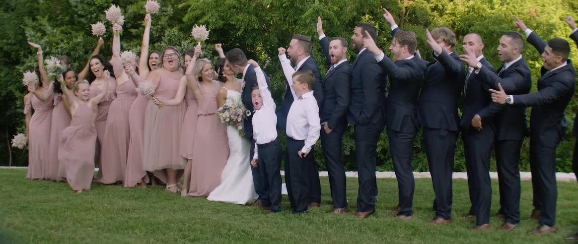 A wedding party cheers while the bride and groom kiss