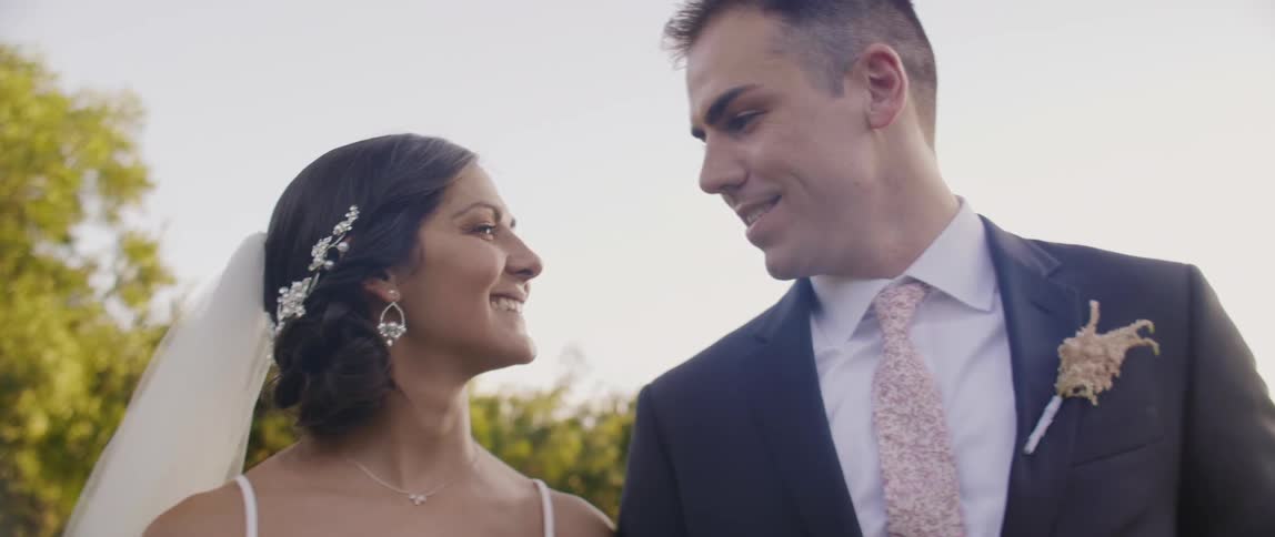Bride and groom are standing outside and smiling at each other