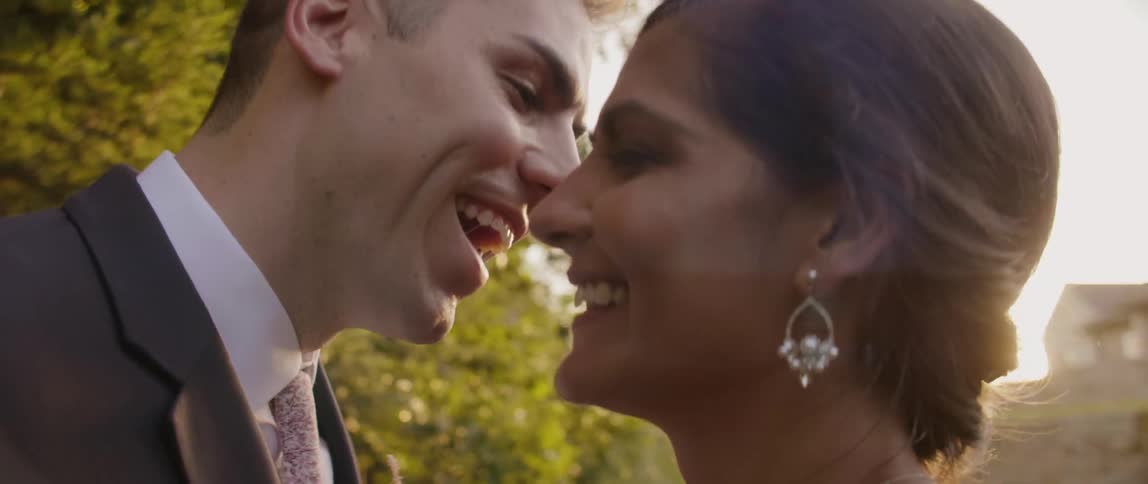 Bride and groom are smiling and embracing outside on sunny day