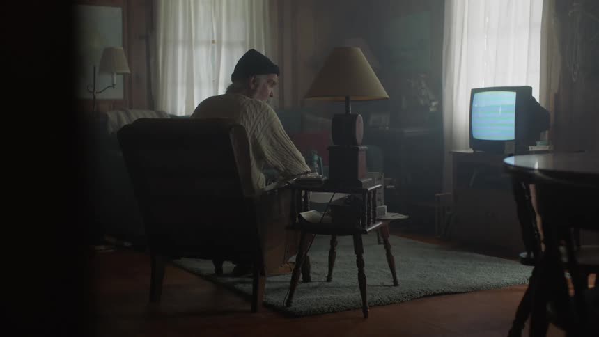 An old man is sitting in his living room watching a television in daylight