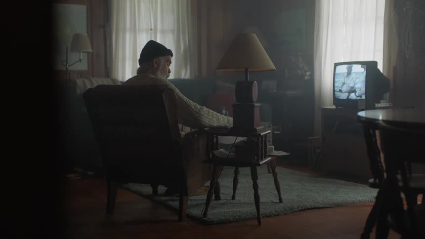 An elderly man watches television in the living room