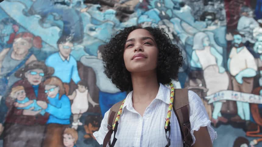 A woman carrying a camera is standing in front of a mural in daylight