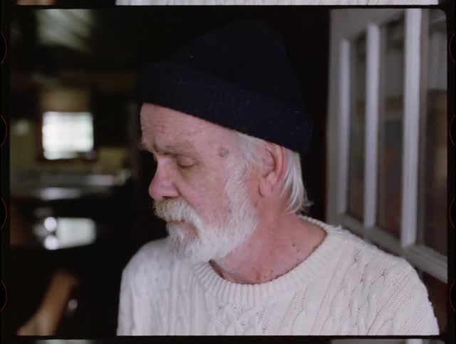 An elderly man looks sad while looking out a front door