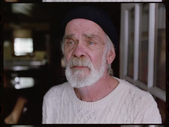 An elderly man looks sad while standing in a doorway
