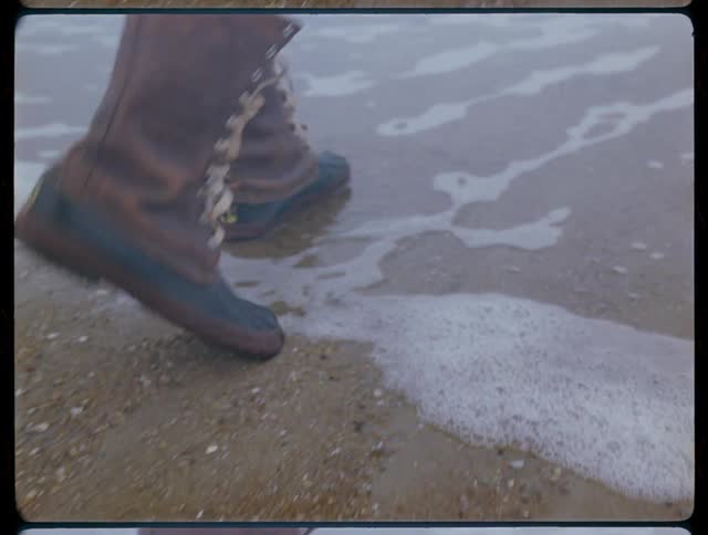 Man walks on a sandy beach in boots