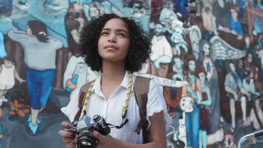 A young woman takes a photograph outside by the graffiti