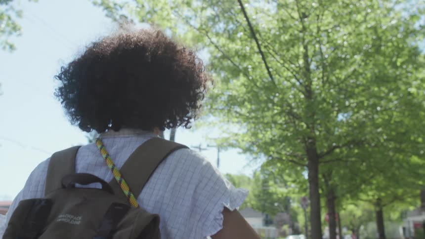 A woman carries a backpack and pushes a bicycle outside