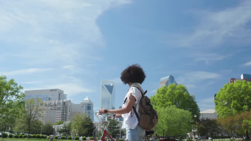 Woman standing next to bicycle while looking at city buildings