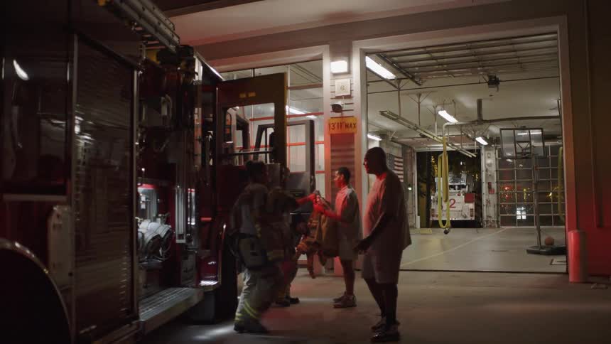 Firemen greet other firemen that walk out of a fire truck at night