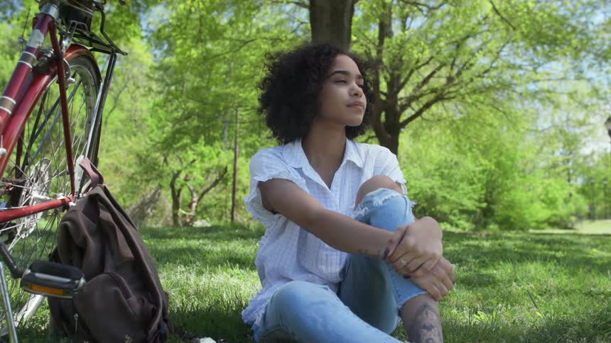 A young woman sits in the grass on a sunny day