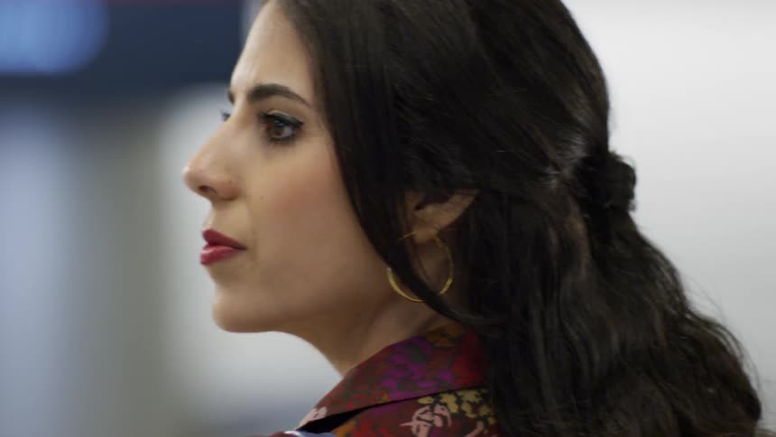 Dark-haired woman looking a back and forth and then smiling and walking towards what she sees