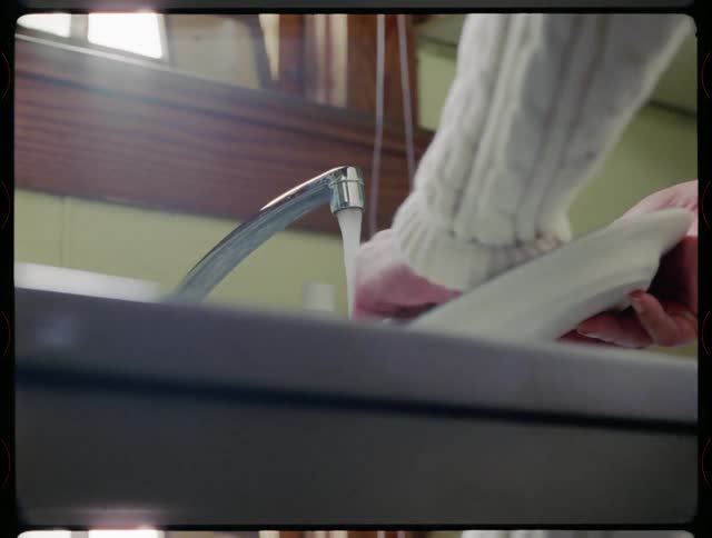 Woman is washing a plate in kitchen sink
