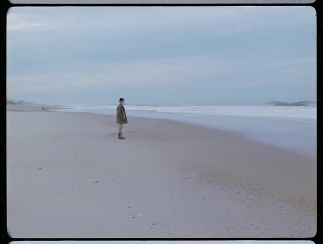 Man is standing on sand beach and staring out at the ocean waves
