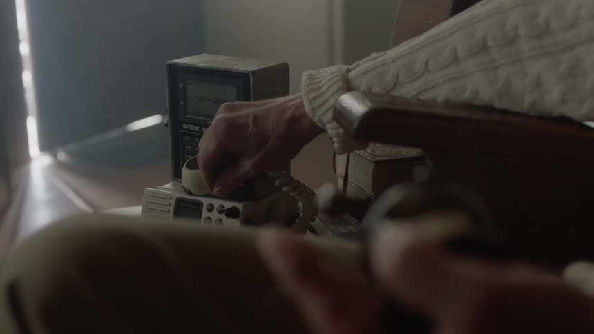 Man turning a device and then adjusting a knob on another device as he sits in a chair