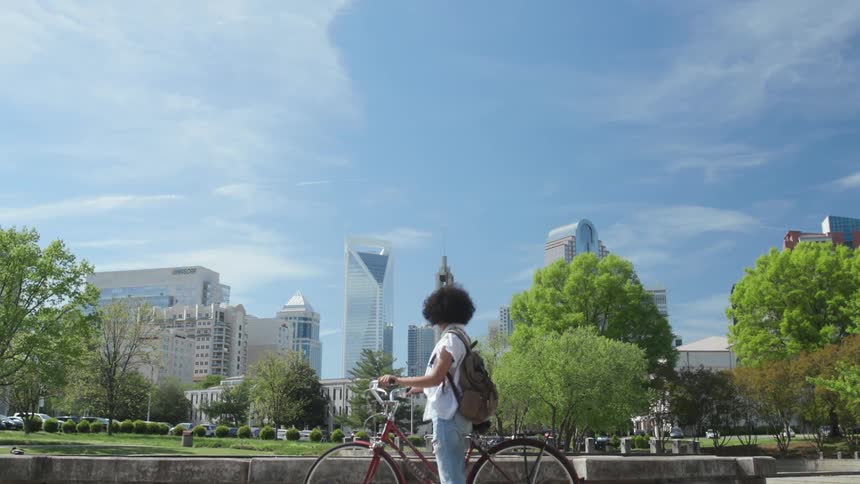 A woman is straddling her bicycle as she takes in a view of a city on a sunny day
