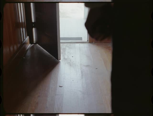 A person stands inside a house near an open door clenching his fist