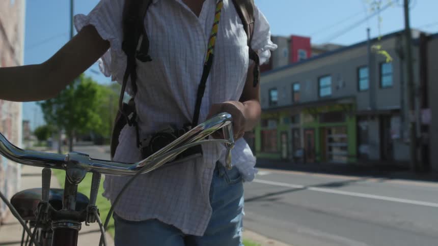 A woman walks her bike on the sidewalk