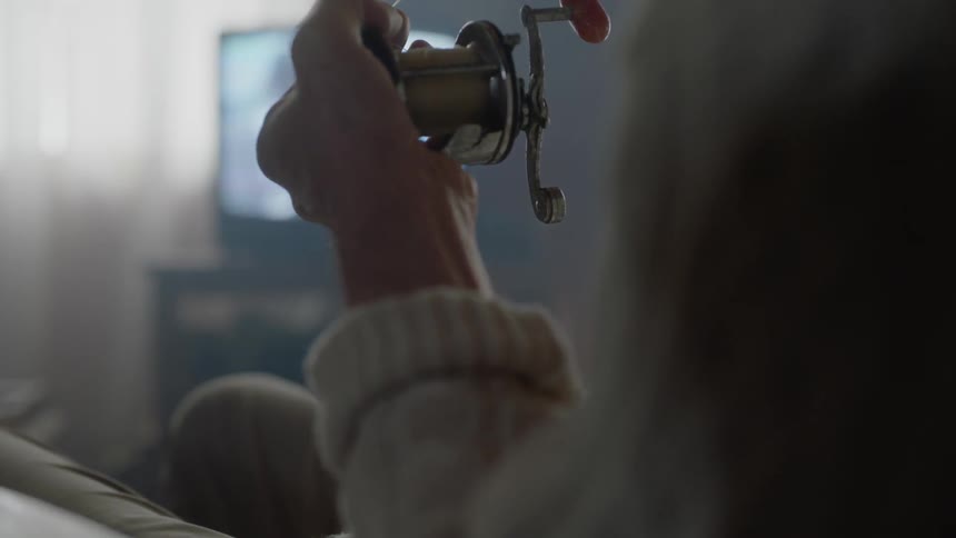 A woman sitting in a chair at home winding a fishing rod