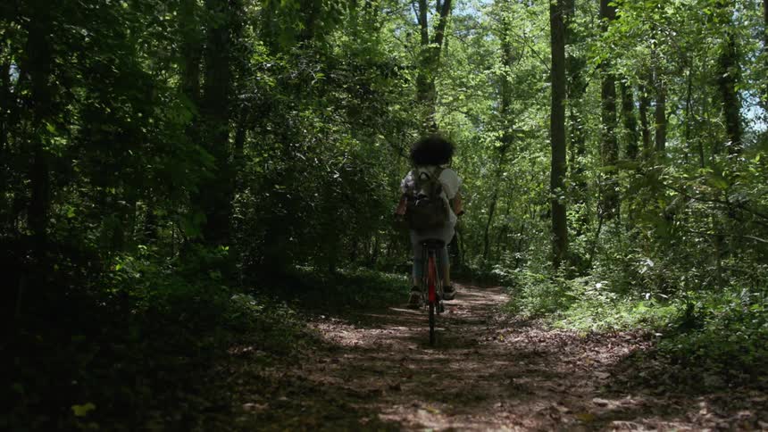 A girl rides a bicycle on a trail through the trees