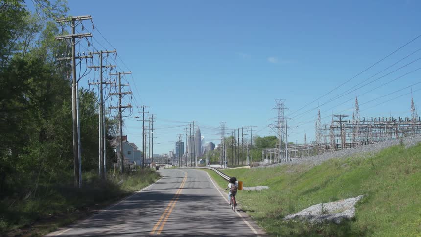 Woman bicycling down the road near a city during the day