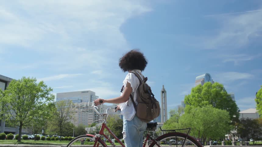 Woman stands next to her bicycle as she looks at a park