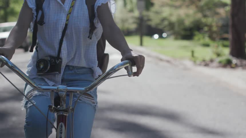 Woman wearing camera is riding bicycle down neighborhood street