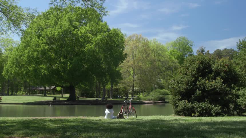 A young woman sits in the grass by the pond