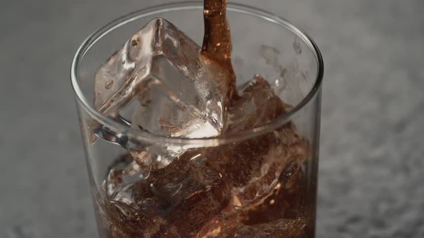 A beverage is poured into a glass with ice cubes