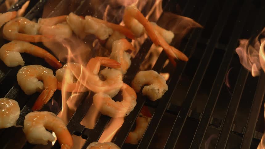 Shrimp being thrown over a grill on open flame