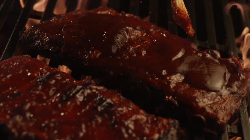 Bbq sauce being added to ribs over open flame