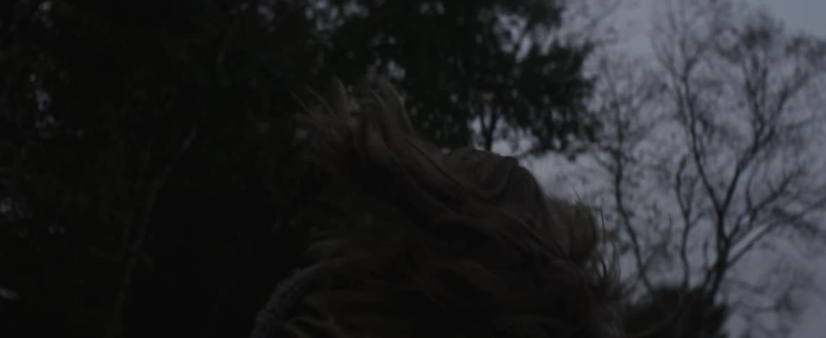 A woman jogs towards trees while her hair bounces