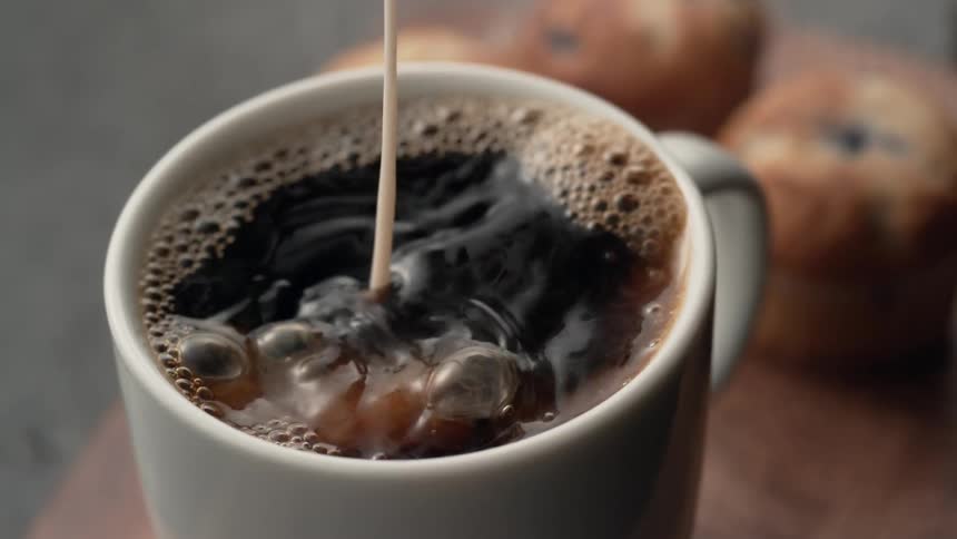 Cream is being poured into coffee in a cup