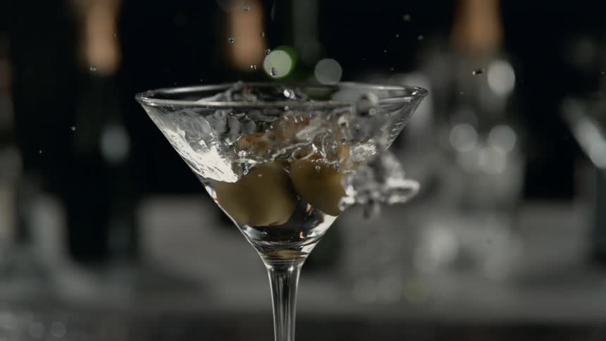 Olives are dropped into martini in slow motion