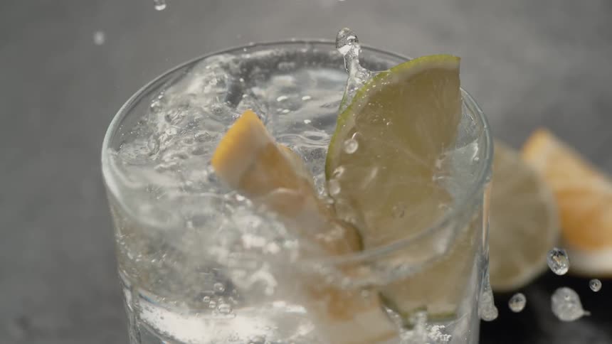 A cup of seltzer water in ice with lemon and lime being thrown in